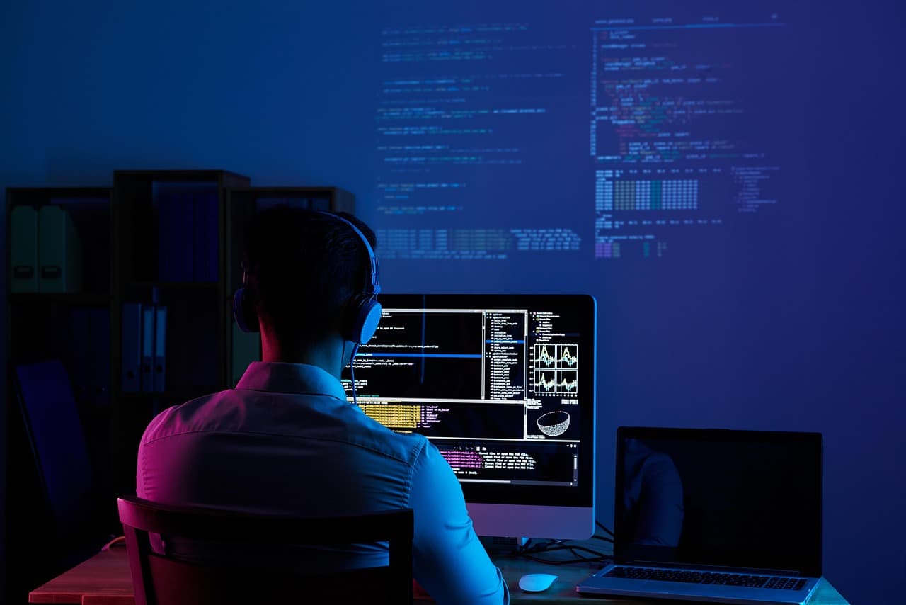 A software developer working at a multi-monitor desk setup reviewing code, the workflow Cursor Origin is designed to restructure around AI agents