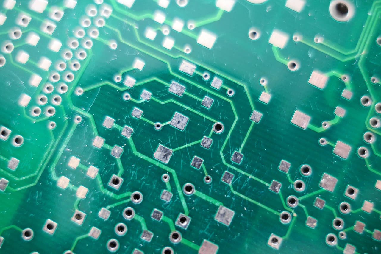 Close-up of a green printed circuit board where copper traces branch between contact pads, a visual metaphor for the fast branching decisions TypeSafe Jev makes inside software